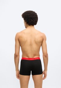 Μαύρα μπόξερ με κόκκινη ζώνη μέσης που φέρει το λογότυπο "TOMMY HILFIGER", παρουσιάζοντας λείο υφή και εφαρμοστή σχεδίαση.