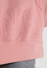 Tissu rose avec lettres en relief formant le mot "NIKE", associé à un vêtement gris sous l'ourlet.