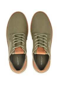 Zapatos de lona verde oliva con punta redonda, diseño con cordones, acentos de cuero marrón y suela de goma texturizada. Logo de GANT en la plantilla.