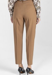 Brązowe spodnie zwężane o gładkiej fakturze, z tylną kieszenią, zestawione z czarnymi szpilkami.