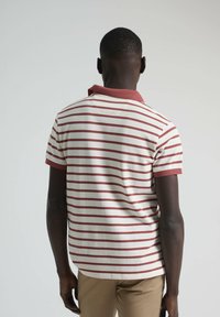 Polo de manga corta en color blanco roto con rayas rojas, con un cuello rojo a contraste y un diseño de dobladillo recto.