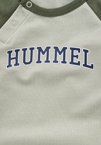 Kortærmet t-shirt i lysegrøn bomuld, der har en mørkegrøn raglanærme og en marineblå "HUMMEL" tryk på brystet.