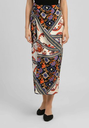 Femme portant une jupe midi taille haute avec des motifs floraux et géométriques colorés, associée à des ballerines noires et un haut noir.