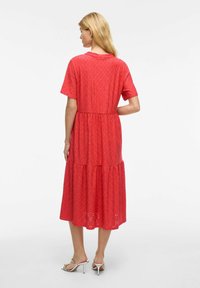 Robe en coton rouge à œillets avec des manches courtes, taille empilée et longueur jusqu'au mollet. Présente une texture crantée et des découpes subtiles.
