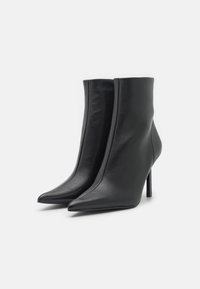 Une paire de bottines en cuir noir avec des pointes effilées et des talons aiguilles fins sur un fond blanc.