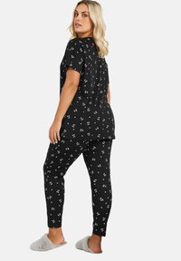 Svart pyjamas set bestående av en t-shirt med kort ärm och smalare byxor, prydd med ett vitt körsbärsblomsmönster. Mjuk tyg, avslappnad passform.