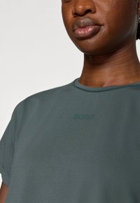 Sötétzöld, rövid ujjú póló, kerek nyakkivágással és texturált anyaggal. A mellkason az "BORG" szó hímzéssel szerepel.