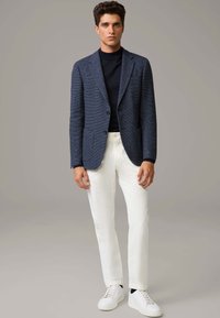 Marineblau strukturierter Blazer mit Reverskragen, weiße Baumwollhose und weiße Sneaker. Minimalistisches Design, gerade Passform und dezente Details.