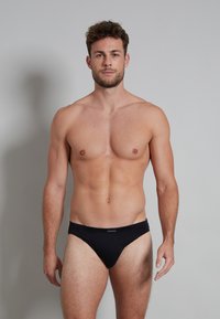 Schwarze Baumwollslips mit einem niedrigen Bund und einer glatten, weichen Textur. Das Design sitzt eng und bietet minimale Bedeckung.