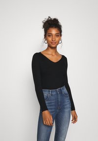 Haut noir à manches longues côtelé avec un décollet�é en V, associé à un jean bleu taille haute. Le haut présente une coupe ajustée et une texture douce.