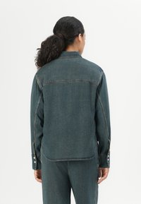 Dunkelblaue Jeansjacke mit Kragen und langen Ärmeln. Verfügt über Stickdetails und Knopfakzente an den Ärmeln. Rückansicht gezeigt.