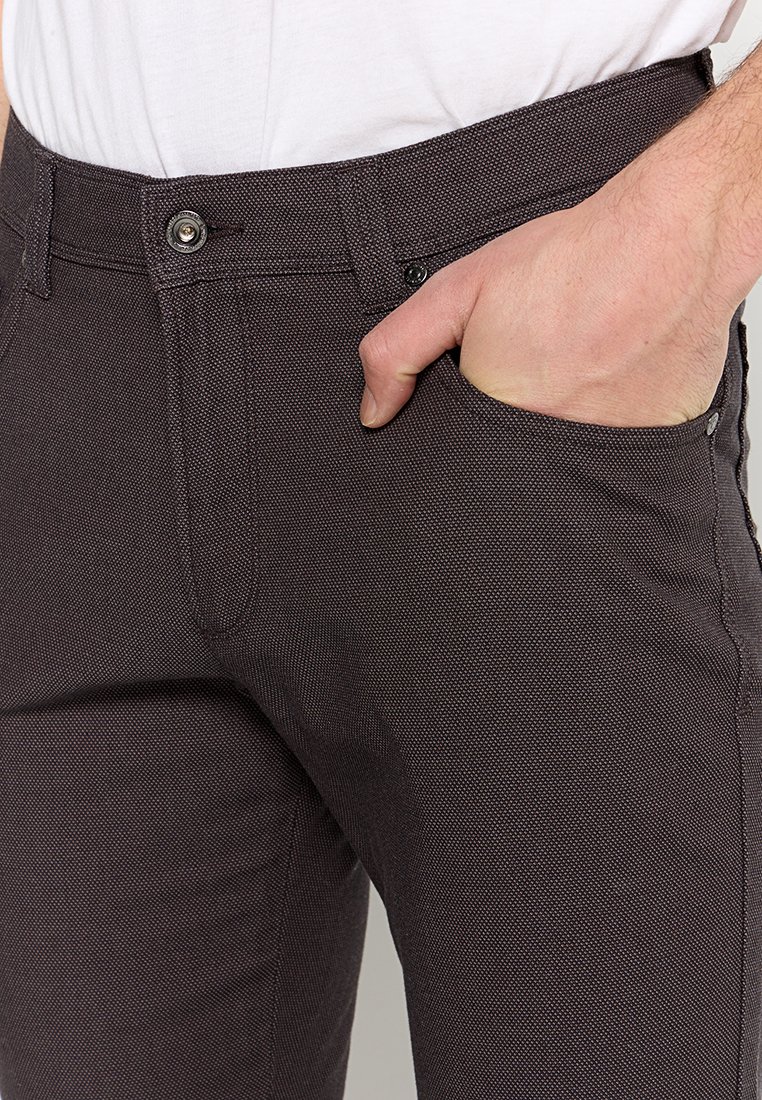 Braune, strukturierte Hosen mit schmaler Passform, ausgestattet mit Seitentaschen und einem Knopfverschluss an der Taille. Dezente Muster sind auf dem Stoff sichtbar.