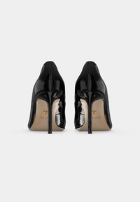 Décolleté in pelle verniciata nera con punta affusolata, tacco a stiletto e logo in oro in rilievo sulla soletta beige.