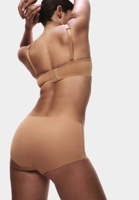 Conjunto de sujetador y pantalones cortos en tono nude, fabricado en una tela suave. El sujetador tiene tirantes ajustables y un diseño sin costuras, mientras que los pantalones cortos son ajustados y de tiro bajo.