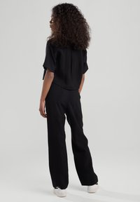 Mustapaita, jossa on lyhyet hihat ja rento malli, yhdistettynä korkeavyötäröisiin mustiin leveälahkeisiin housuihin ja valkoisiin tennareihin.