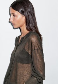 Dunkelolivgrüner, transparenter Strickpullover mit knöpfbarem Ausschnitt, langen Ärmeln und umgeschlagenen Manschetten, verfügt über einen lässigen Schnitt und eine weiche Textur.