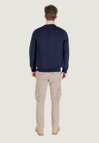 Maglione di lana blu navy con scollo rotondo, indossato con pantaloni cargo beige dotati di più tasche e un piccolo logo, visto da dietro.