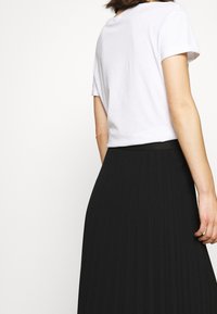 Hvid kortærmet T-shirt parret med en sort plisseret maxiskørt, der fremhæver en tydelig tekstur og bevægelse i stoffet.