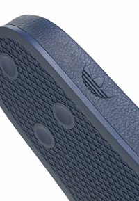 Semelle en caoutchouc bleue avec motif de grip texturé et deux indentations circulaires, avec un logo Adidas trefoil embossé sur le bord latéral.