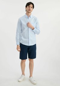 Jasnoniebieska koszula w kratkę z kołnierzykiem zapinanym na guziki, z podwiniętymi rękawami, zestawiona z granatowymi szortami. Całość uzupełniają białe trampki. Prosty i swobodny strój.