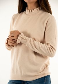 Lichtroze trui met een gerimpelde halslijn, textuur met kleine verhoogde stippen, en versierd met knoopdetails op de gerimpelde manchetten.