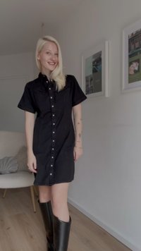 Vestido negro de botones con mangas cortas, que presenta un diseño ajustado y bolsillos en el pecho. Lleva botas negras hasta la rodilla.