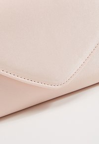 Pochette rose clair à finition satinée, avec un rabat triangulaire, des coutures discrètes et une texture lisse.