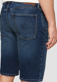 Donkerblauwe denim shorts met een rechte snit, zichtbare achterzakken en subtiele stikseldetails. De tailleband heeft een bruine leren patch.