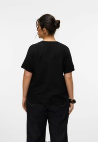Camiseta de algodón negra con mangas cortas, escote redondo y un corte relajado, combinada con pantalones de mezclilla oscuros; la vista posterior muestra un diseño simple.
