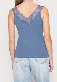 Blå ribbad linne med ett spetsdetalj i V-ringning. Har en figurnära passform och är parat med ljusblå högmidjade jeans.