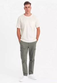 Herrecreme t-shirt med korte ærmer og brystlomme, parret med olivenfarvede cargo-bukser med sidelommer. Hvide sneakers fuldender looket.
