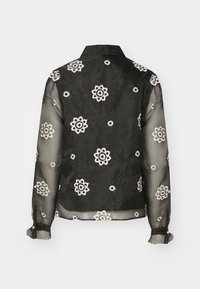Bluză neagră transparentă cu broderie florală albă, având un guler clasic și manșete cu nasturi, evidențiind materialul și designul delicat.