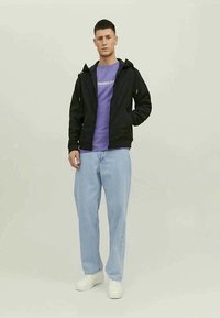 Veste zippée noire sur un T-shirt violet avec du texte blanc, associée à un jean droit bleu clair et des baskets blanches.