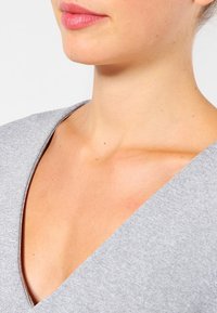 Harmaa V-pääntiepaita pehmeällä tekstuurilla, tiukalla muotoilulla ja leveällä kaula-aukolla, joka korostaa sileää ihoa ja luonnollista sävyä.