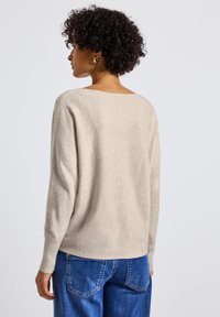 Hellbeige gestrickter Pullover mit lässiger Passform, rundem Halsausschnitt und gerippten Bündchen. Getragen mit hochtaillierten blauen Jeans.