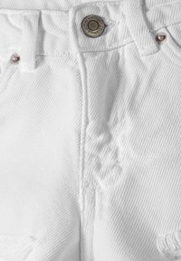Jeans de mezclilla blanca con un tejido texturizado, un cierre de botón metálico y detalles de costura visibles cerca de la cintura y los bolsillos.