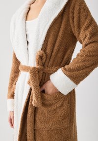 Brown, plush bathrobe with white collar and cuffs, featuring a tied waist, two side pockets, and soft texture throughout.