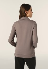 Top grigio heathered a maniche lunghe con colletto alto, texture morbida e design aderente. Orlo leggermente curvato sul retro. Abbinato a pantaloni neri.