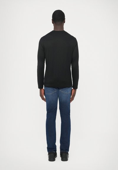 Fekete hosszú ujjú ing, testhez simuló szabású, sima tapintású, kék farmernadrággal párosítva, egyenes szárú szabás, fekete cipővel, hátulnézetben.