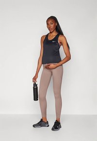 Schwarzes sportliches Tanktop mit pinken Akzenten, beigefarbene Leggings, schwarze Turnschuhe und eine schwarze Wasserflasche, getragen von einer schwangeren Person.