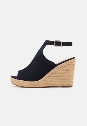 Sort åben tå kile-sandal med flettet jutefod og justerbar ankelrem med sølvspænde på hvid baggrund.