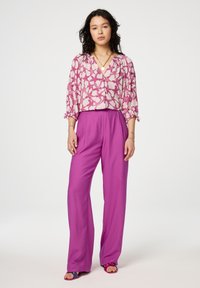 Roze gebloemde blouse met v-hals en driekwartmouwen, gecombineerd met hooggesneden, wijde paarse broekspijp en bijpassende sandalen.