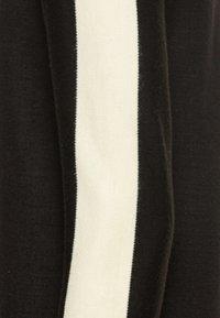 Svart tyg med en framträdande vertikal vit rand. Texturen verkar mjuk och stickad, vilket betonar en enkel, modern design.