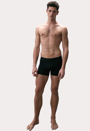 Zwarte boxershorts gemaakt van rekbaar materiaal, met een brede elastische tailleband met de merknaam, die nauw om het lichaam zit.