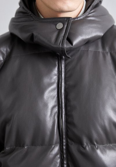 Mörkgrå vadderad jacka i slät läder. Har hög krage, dragkedja och ett tryckknappselement. Texturerad, elegant finish.