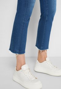 Vita läderplattformssneakers med rund tå och texturerad yta, i kombination med mid-blå denim med fransad fåll och rak benpassform.