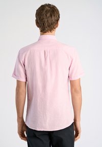 Korte mouwen lichtroze shirt met een kraag, gestructureerde stof en een afgeronde zoom. Heeft een achterplooi en opgerolde mouwen.