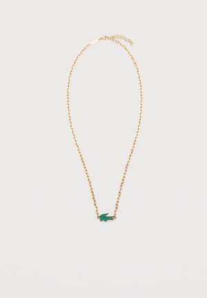 Collana con catenina d'oro e piccolo ciondolo a forma di coccodrillo verde realizzato in pietre su sfondo bianco.