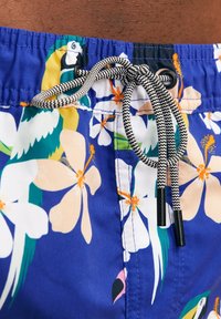 Blauwe zwembroek met een patroon van grote bloemenprints in wit en oranje, voorzien van een zwart-witte trekkoord en oogjes.