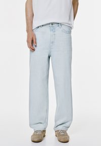 Jeans largi de culoare albastru deschis, cu talie înaltă, având un design cu cinci buzunare și o ușoară decolorare. Asortați cu adidași crem.